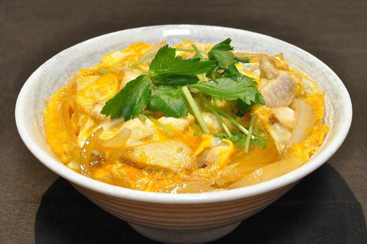 Oyakodon bowl with chicken and softly set egg over rice, topped with green herbs