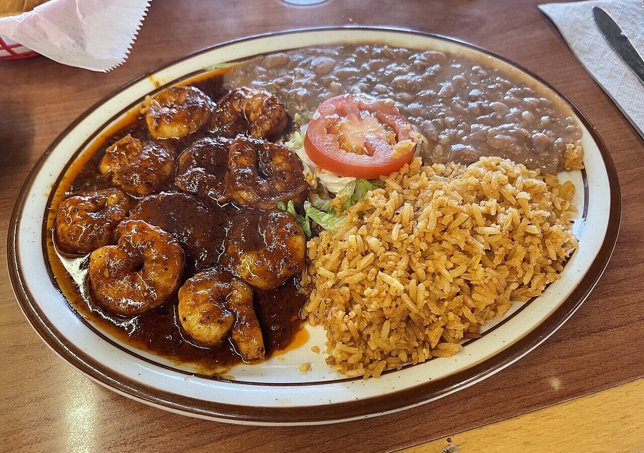 Camarones a la diabla, spicy shrimp in a dark red chile sauce, with rice, refried beans, and tomato