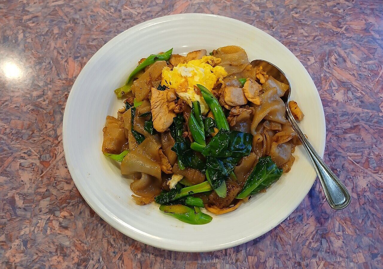 Chicken pad see ew with wide rice noodles, Chinese broccoli, and egg on a white plate