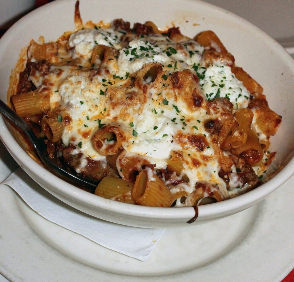 Baked ziti with tomato meat sauce, ricotta, and melted mozzarella in a white bowl