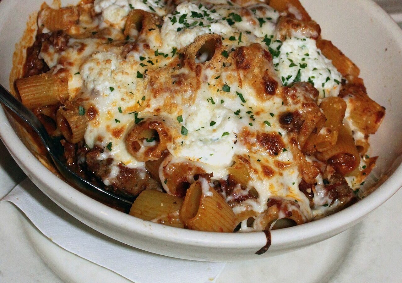 Baked ziti with tomato meat sauce, ricotta, and melted mozzarella in a white bowl