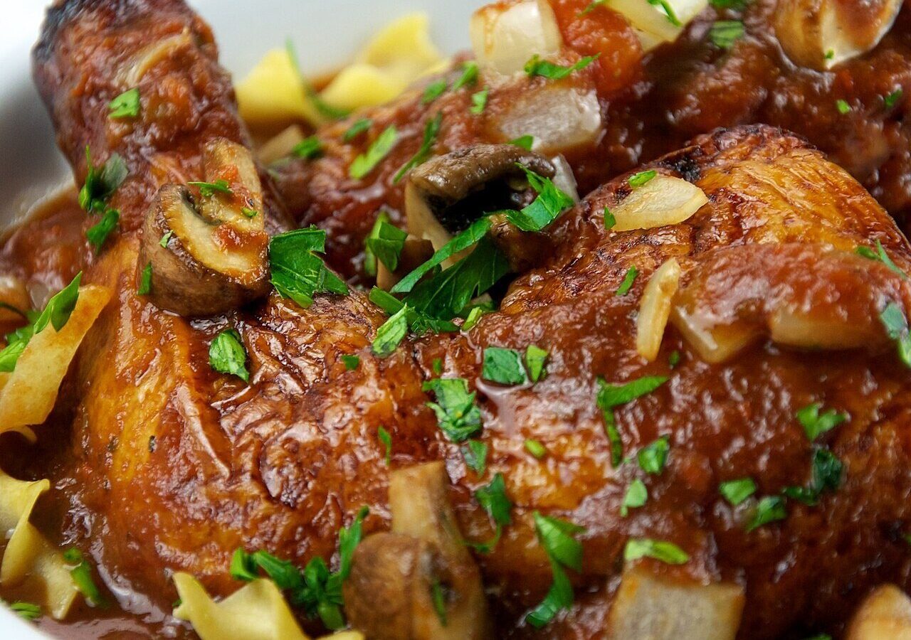 Chicken cacciatore with mushrooms, onions, and tomato sauce over pasta, garnished with parsley