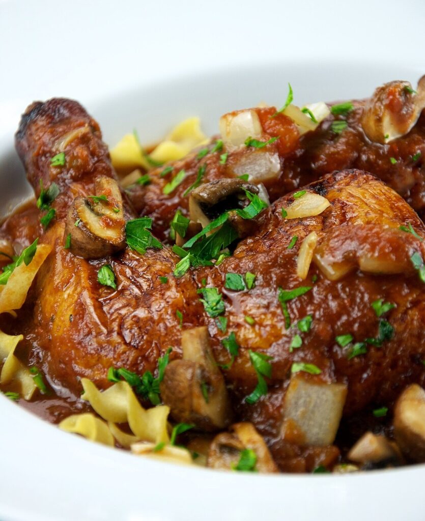 Chicken cacciatore with mushrooms, onions, and tomato sauce over pasta, garnished with parsley