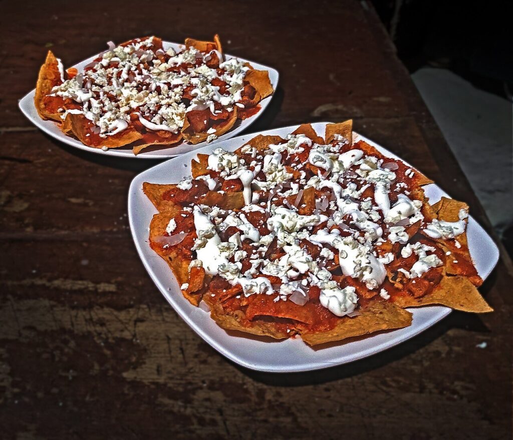 Red chilaquiles topped with crema, crumbled cheese, and onion on white plates