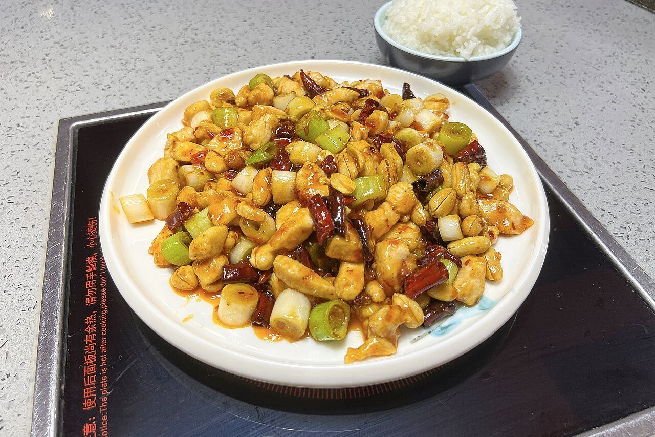 Kung pao chicken with diced chicken, scallions, dried red chiles, and peanuts on a white plate