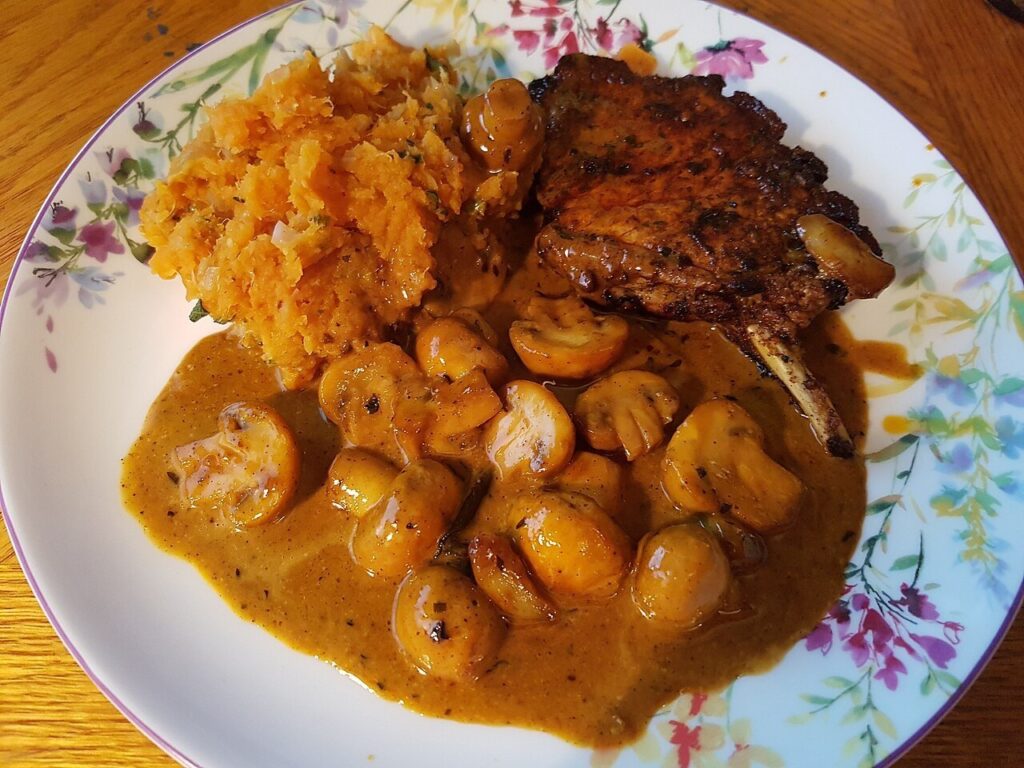Seared pork chop with mushrooms in a creamy gravy beside mashed sweet potatoes