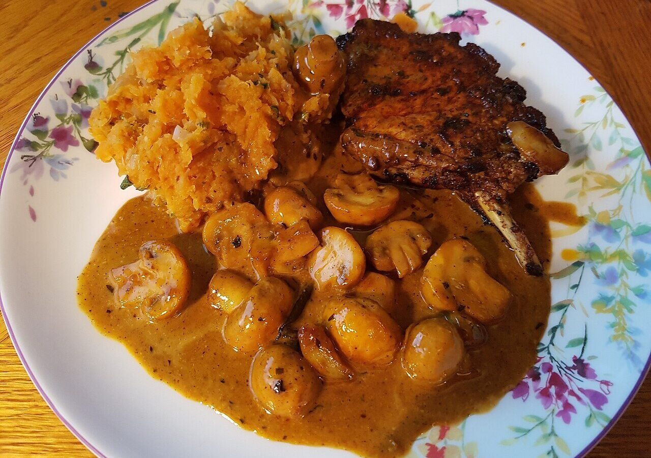 Seared pork chop with mushrooms in a creamy gravy beside mashed sweet potatoes