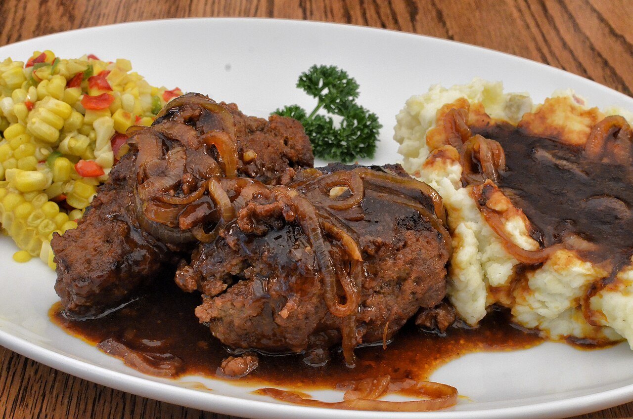 Two Salisbury steaks in brown onion gravy with mashed potatoes and corn