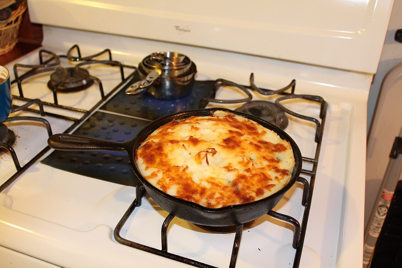 Shepherd's pie with a golden broiled potato and cheese topping in a cast iron skillet on a stove