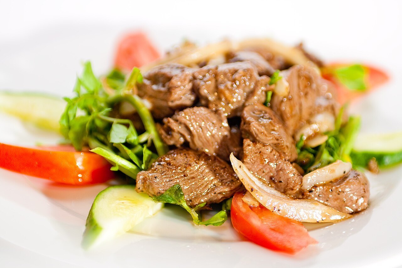 Vietnamese shaking beef cubes with onions over lettuce, tomatoes, and cucumber