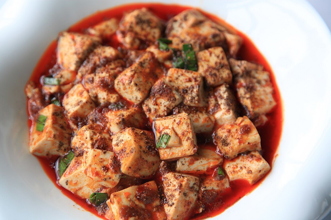 Mapo tofu with cubes of tofu in a glossy red chili sauce topped with chopped scallions